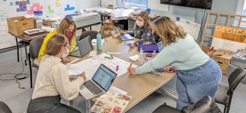 Two educators and two interns are collaboratively working at a large table in the museum's temporary offices, Spring 2022.