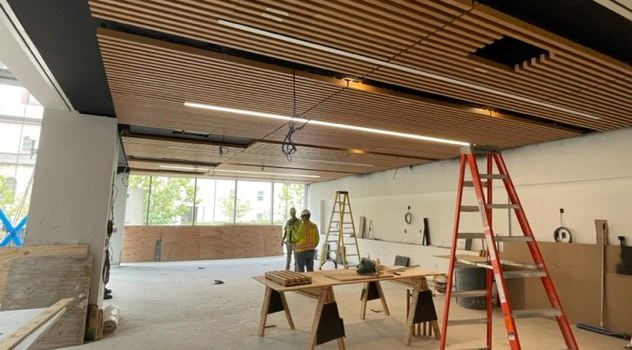 Interior view of the construction site featuring the multipurpose room with workers installing the slatted ceiling.