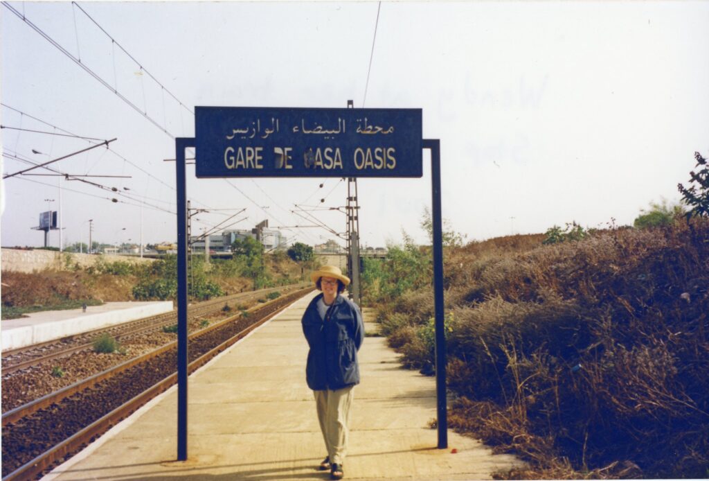 Color photograph of Wendy Schumacher standing at the train station she took to work for the Peace Corps in Casablanca, Morocco, 2001. Lillian and Albert Small Capital Jewish Museum Collection. Gift of Wendy Schumacher