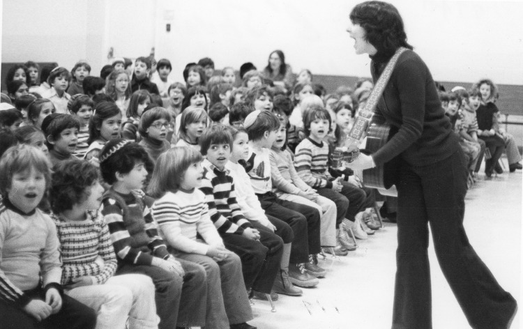 Black and white image of a woman playing guitar in front of a crowd of school children.