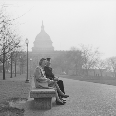 Black and white photo of a couple sitting on a bench in front of the United States Capitol.